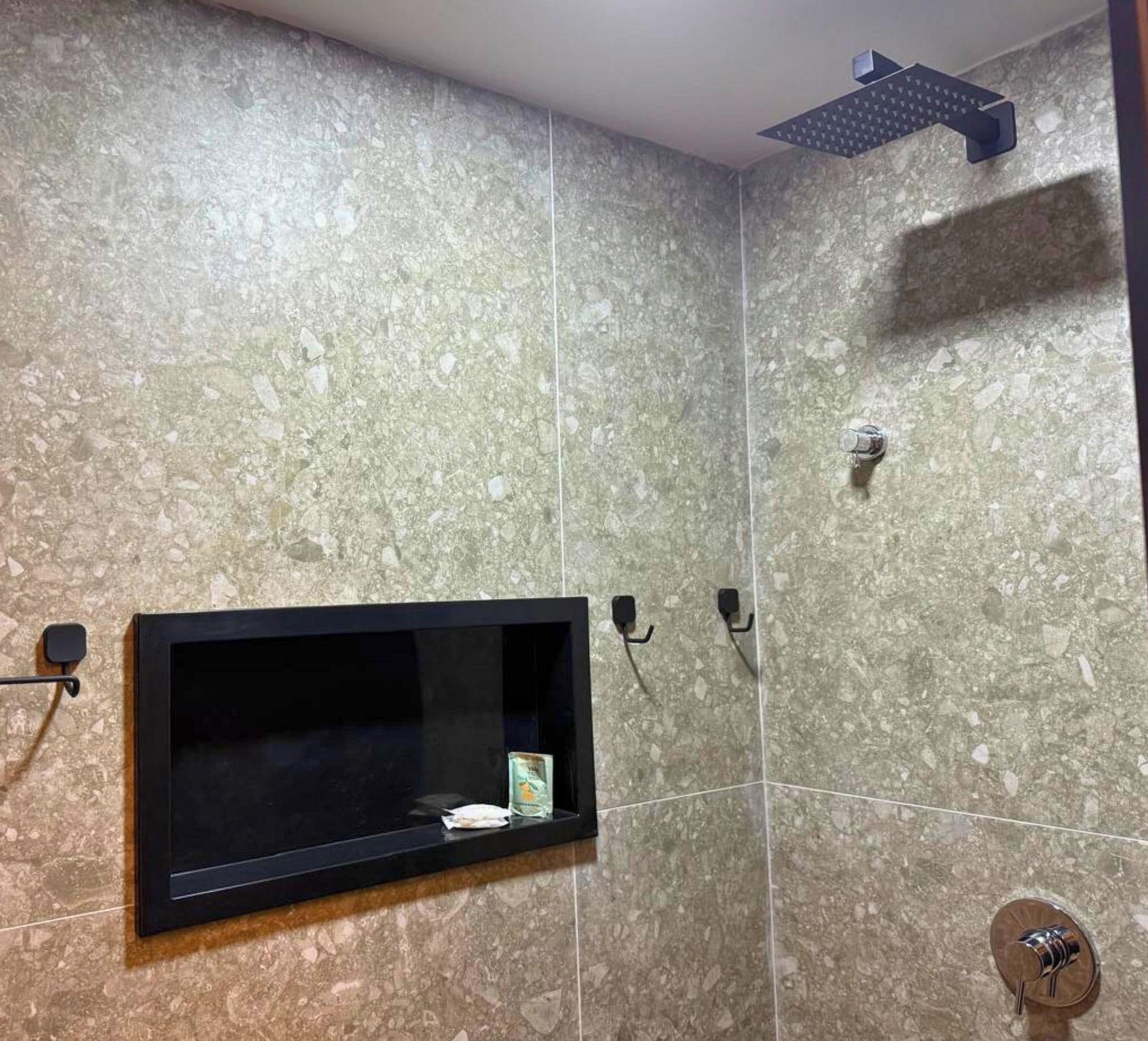 Une salle de bain équipée d’un téléviseur encastré, d’une pomme de douche et d’un porte-serviettes.