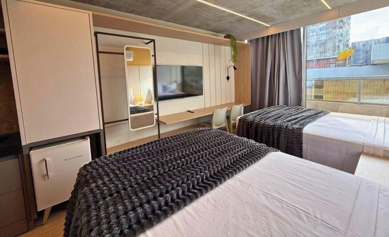 A modern hotel room with a bed, a desk, a television, and a window with a view of the outside.