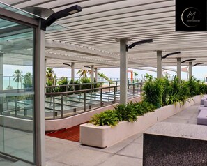 Un área de estar exterior moderna con barandilla de vidrio, asientos y jardineras.