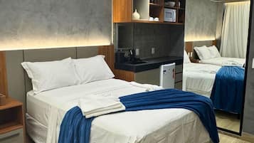 A modern hotel room with a large bed, a small kitchenette, a mirror, and a wooden headboard.