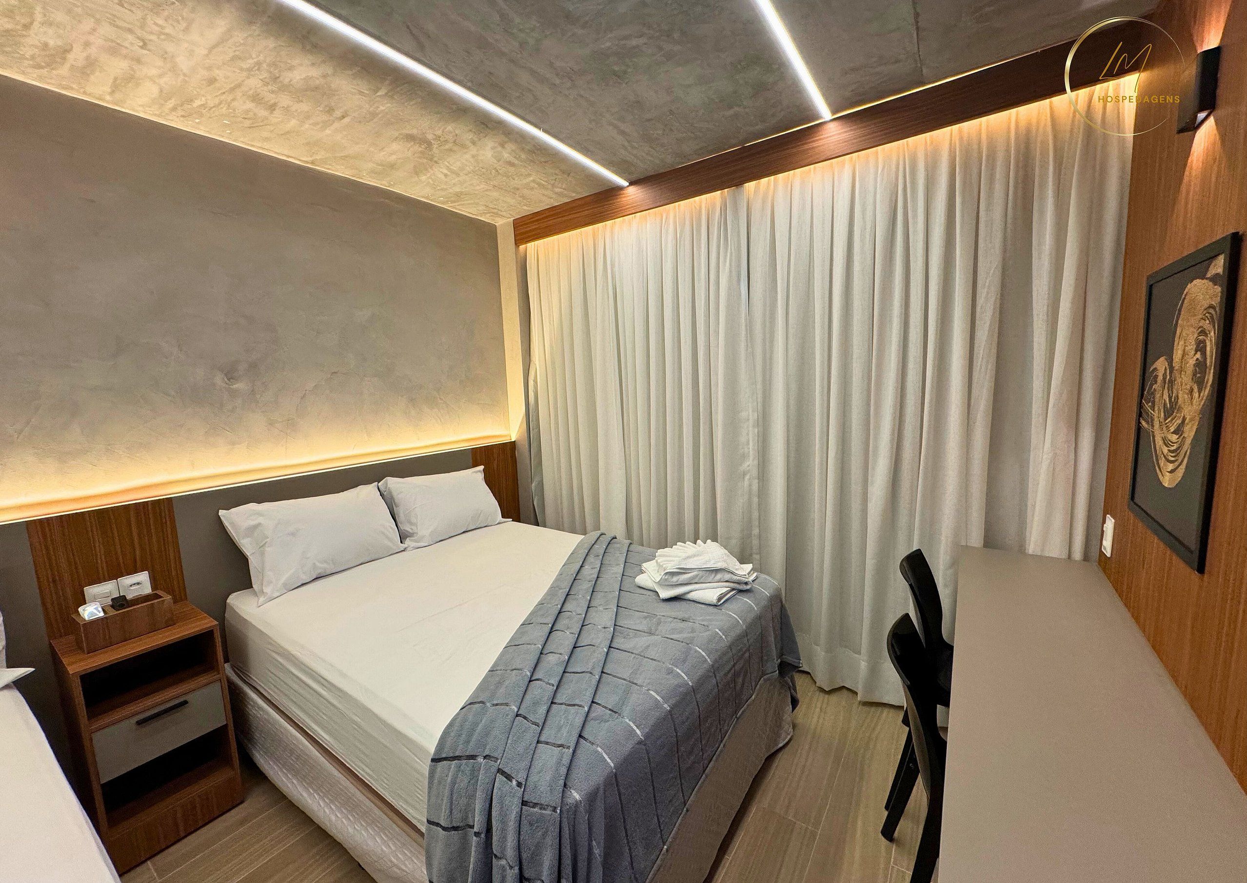 A hotel room with a bed, bedside table, and a chair.