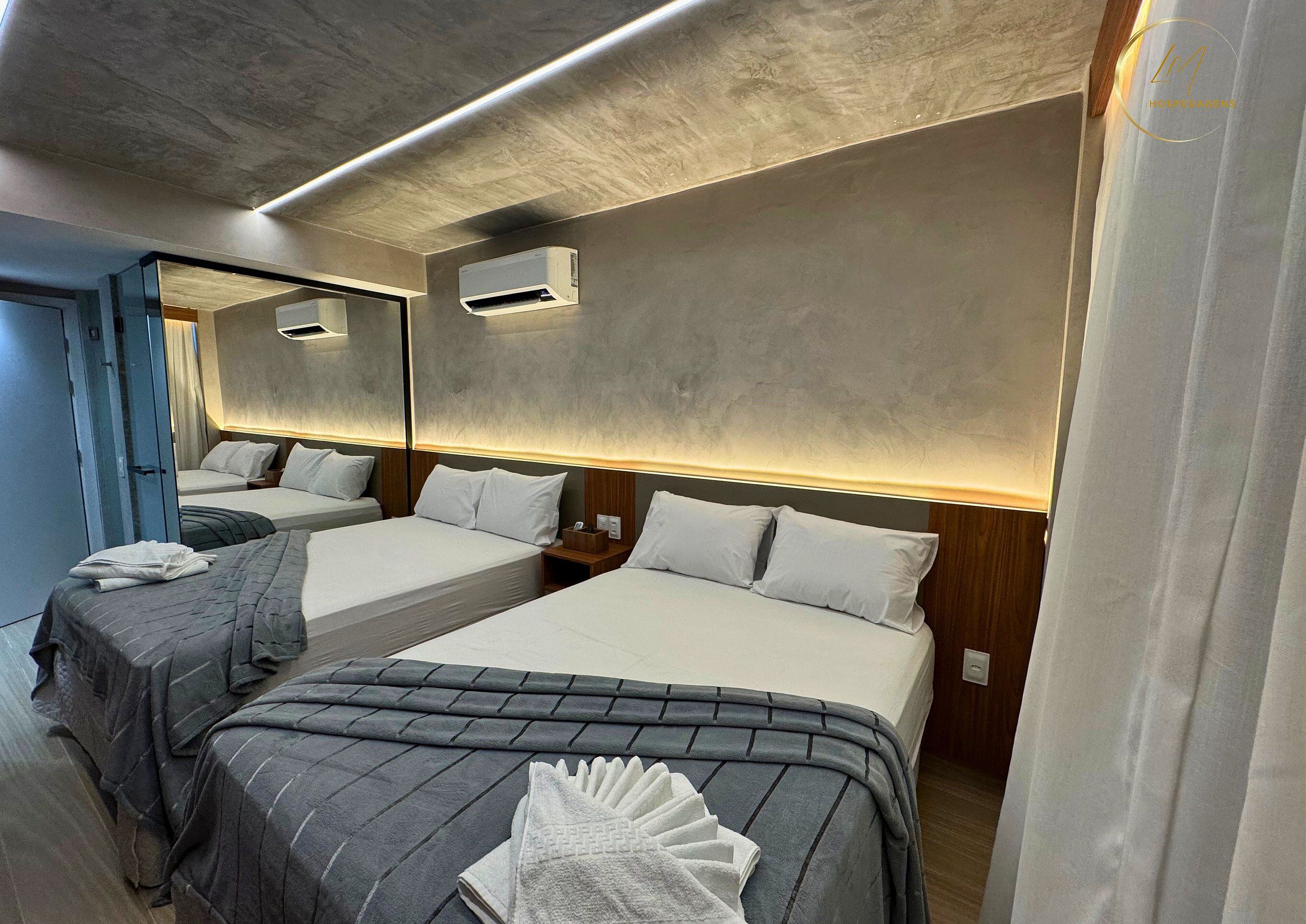 Een hotelkamer met twee bedden, een grote spiegel, een airconditioning en een houten hoofdbord.