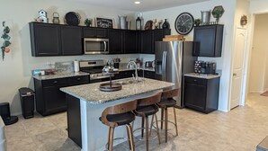 A modern kitchen with dark cabinetry, granite countertops, stainless steel appliances, and a central island with bar stools. - Blue Door Retreat - 
a home in Tartesso, Buckeye, AZ (Buckeye)