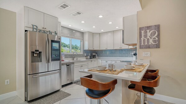 A modern kitchen with stainless steel appliances, a dining area with wooden chairs, and a view of the outdoors.