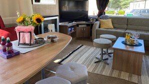 A modern RV interior with a sofa, TV, dining table, and a small kitchenette.