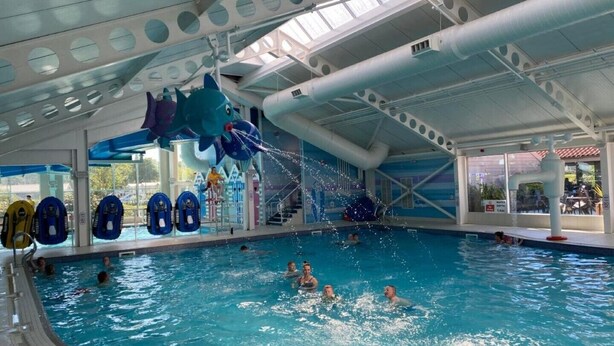 An indoor swimming pool with multiple lanes, a large shark decoration, and several blue water slides.