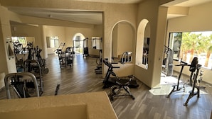 A spacious gym with various exercise equipment, large windows, and a view of palm trees outside. - 2 bedroom condo, marina view in Terrasol Beach Resort, 15 min walk to everything (Cabo San Lucas)