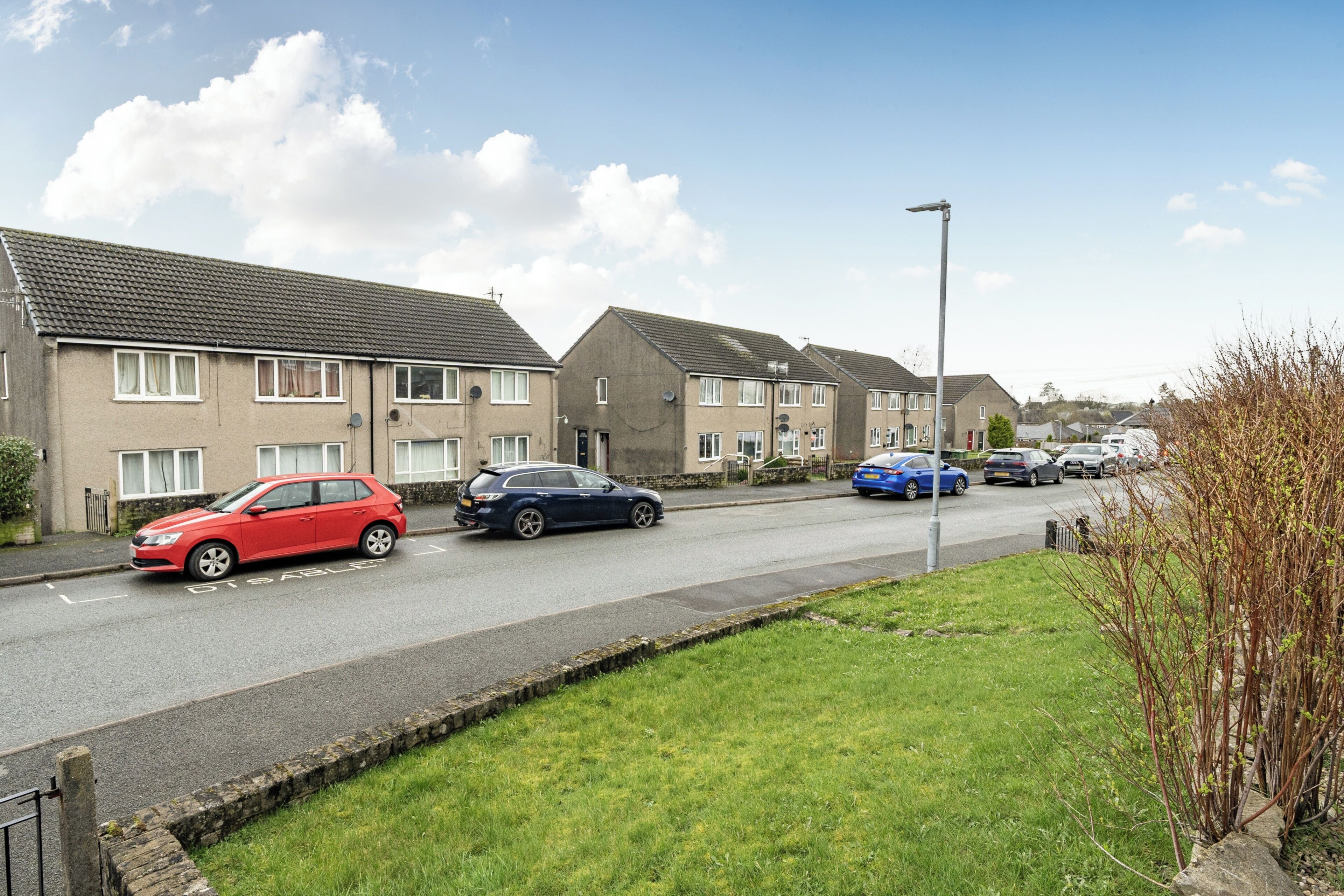 A residential street with houses, a red car, and a blue car parked on the side.