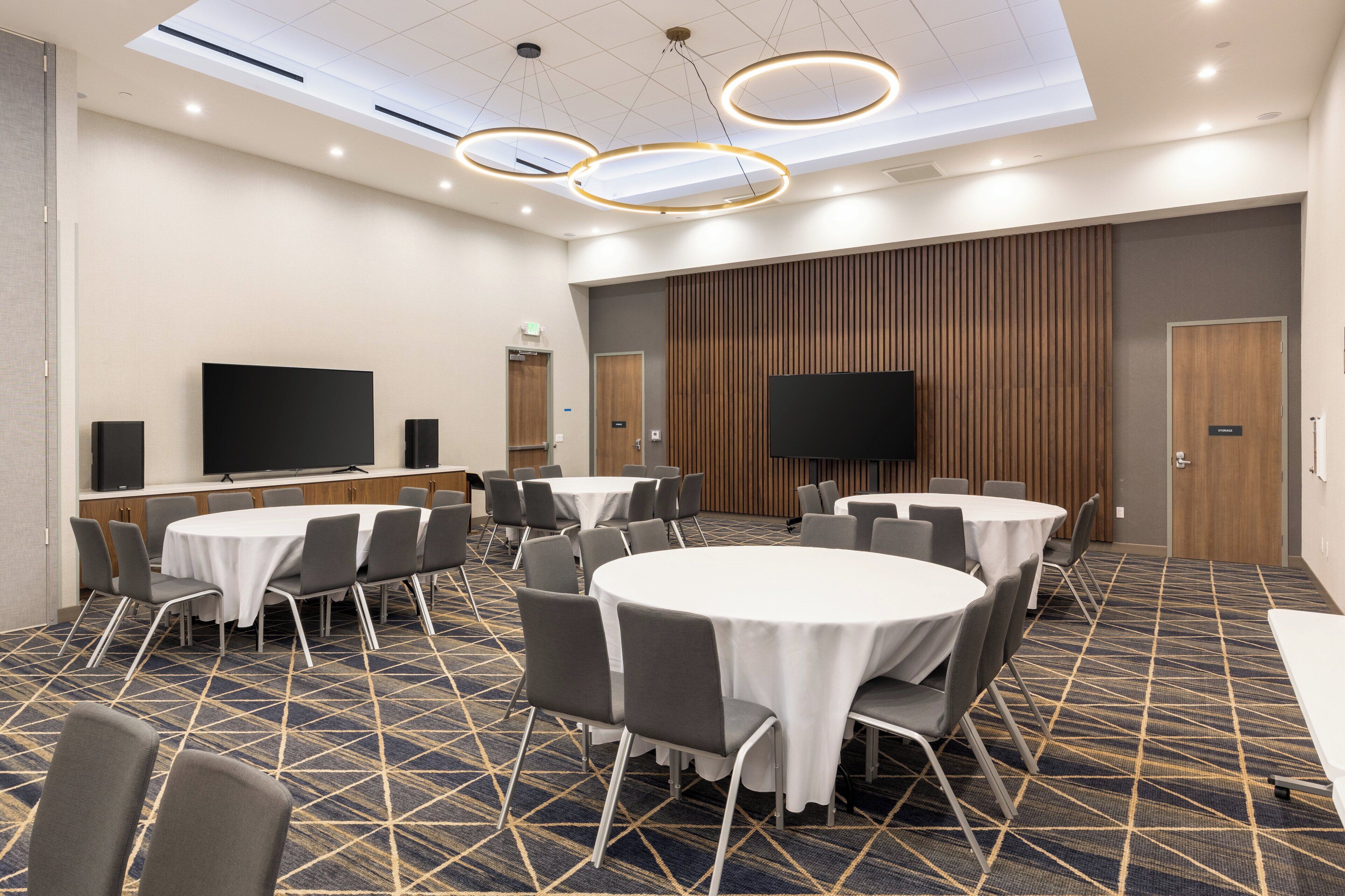 A conference room with round tables, chairs, a large flat-screen TV, and a patterned carpet.