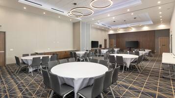 A conference room with round tables and chairs, a flat-screen TV, and a patterned carpet.