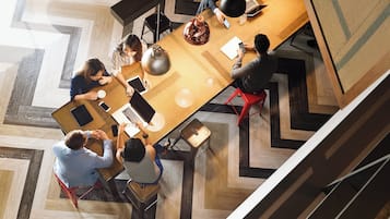 A modern office space with a large wooden table surrounded by people working on laptops and using mobile devices.