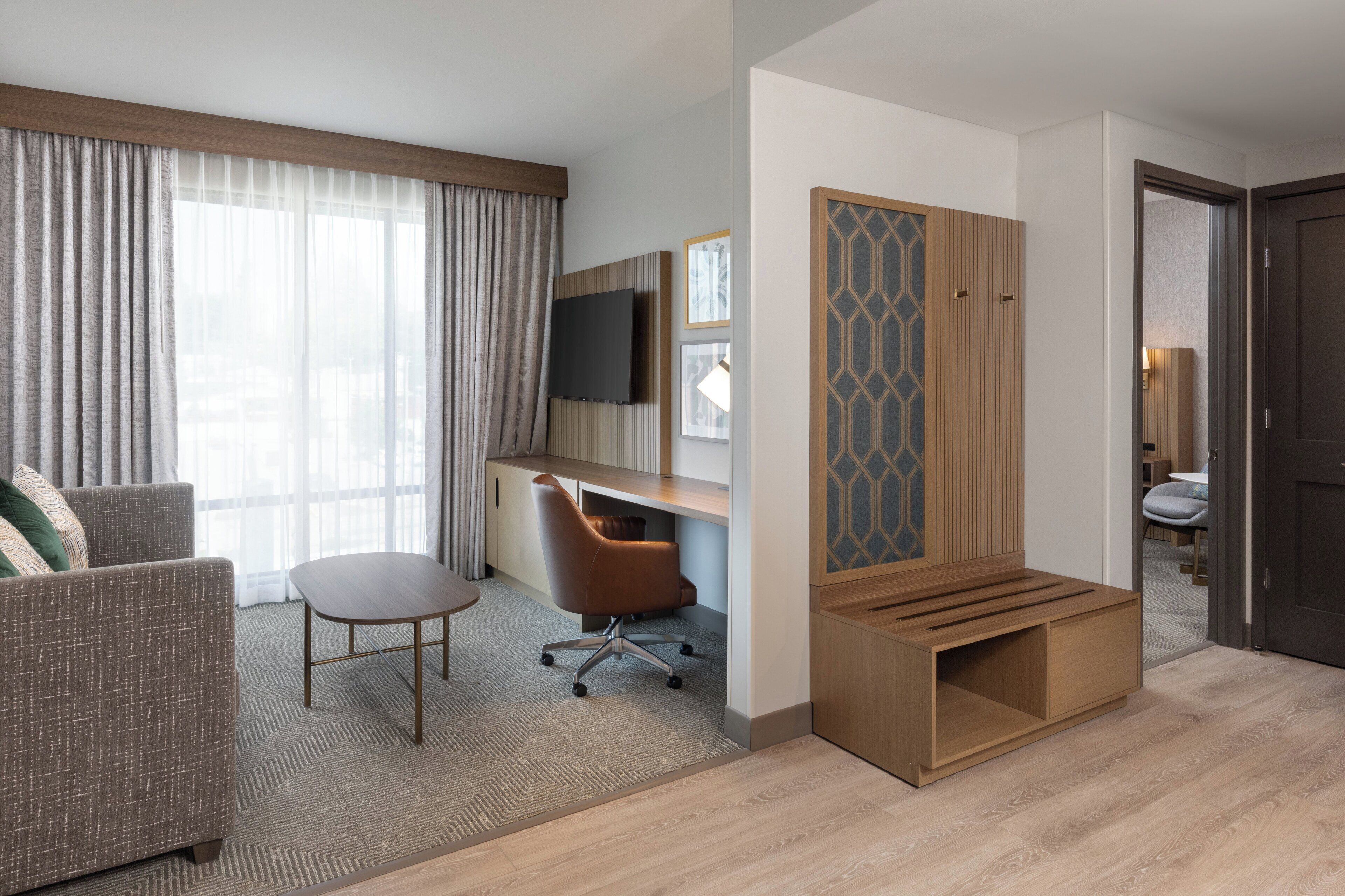 A hotel room with a sofa, a desk, a chair, a TV, and a wooden partition.