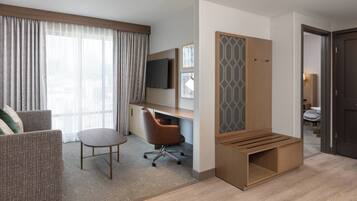 A hotel room with a sofa, a desk, a chair, a TV, and a wooden partition.