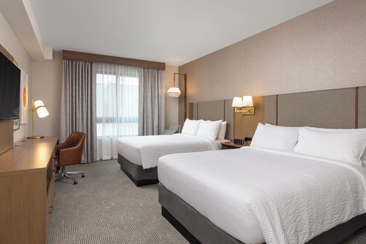 A hotel room with two beds, a desk, a chair, and a television.