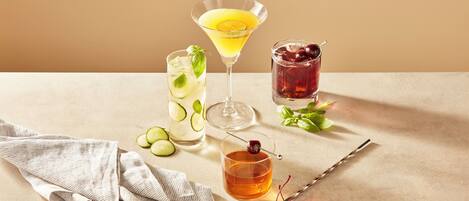A table with three drinks, a cloth napkin, and a spoon with cherries.