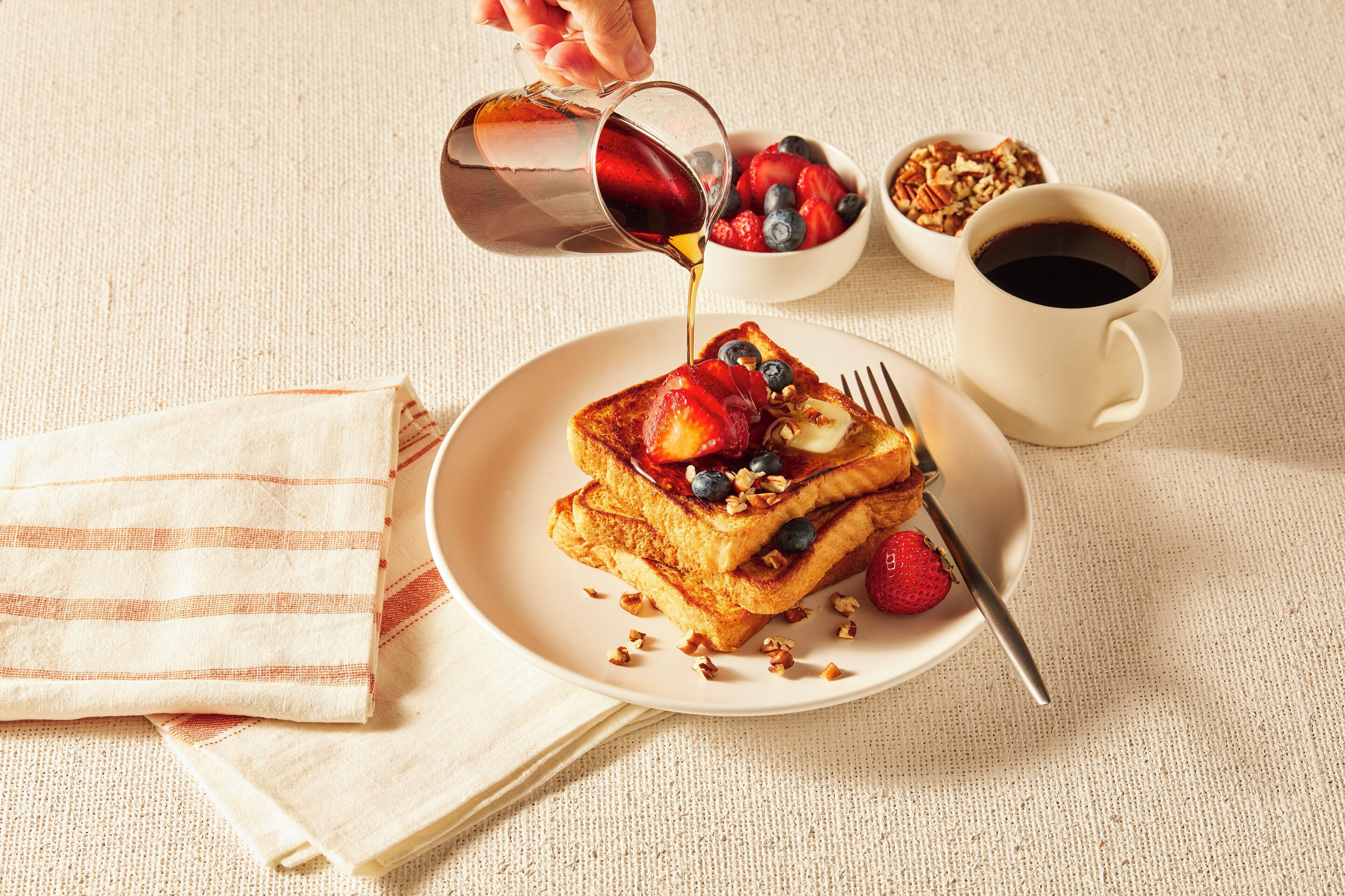A breakfast setting with French toast, berries, and a cup of coffee on a table.