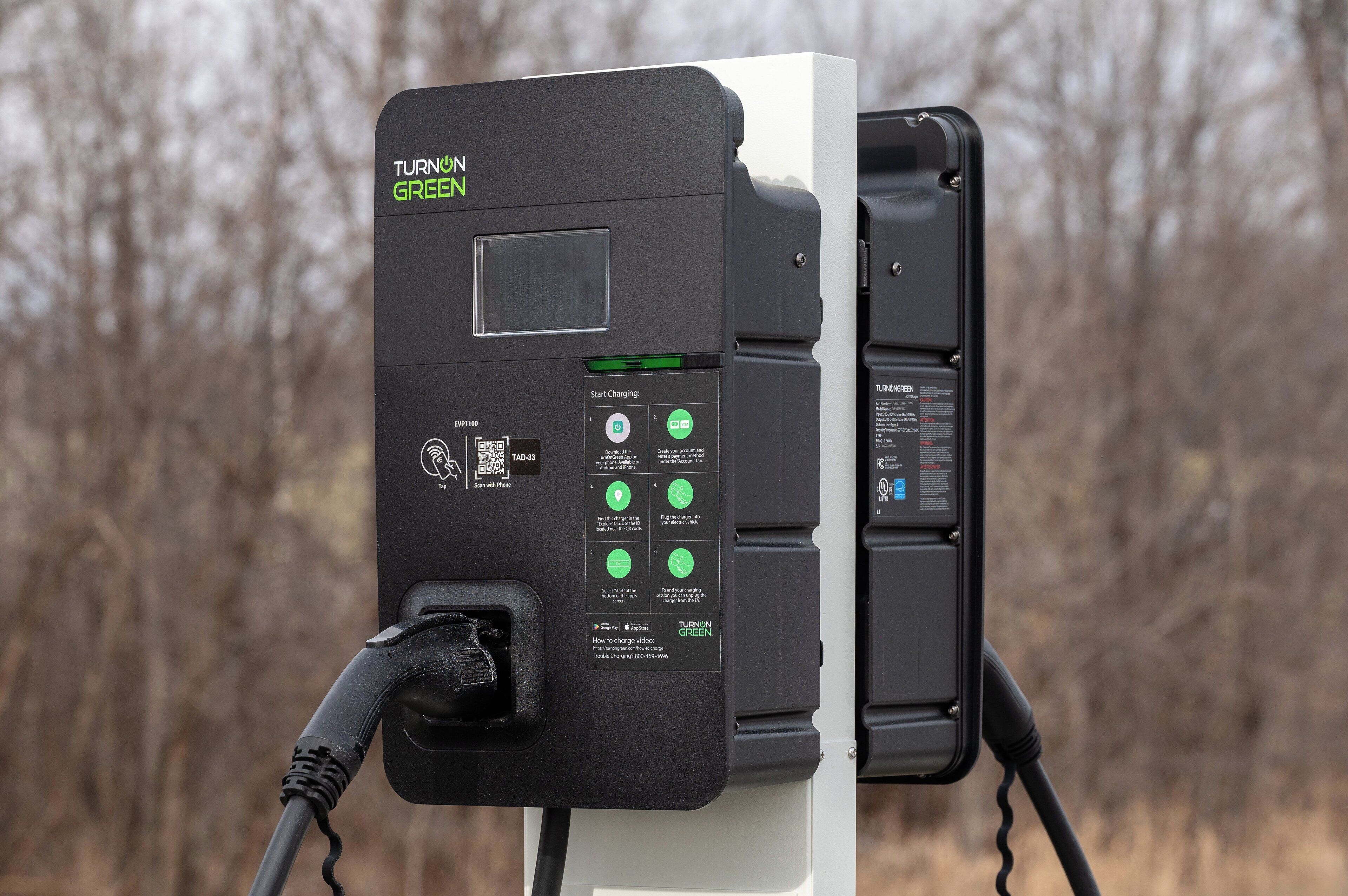 A charging station with a display and instructions, set against a backdrop of leafless trees.