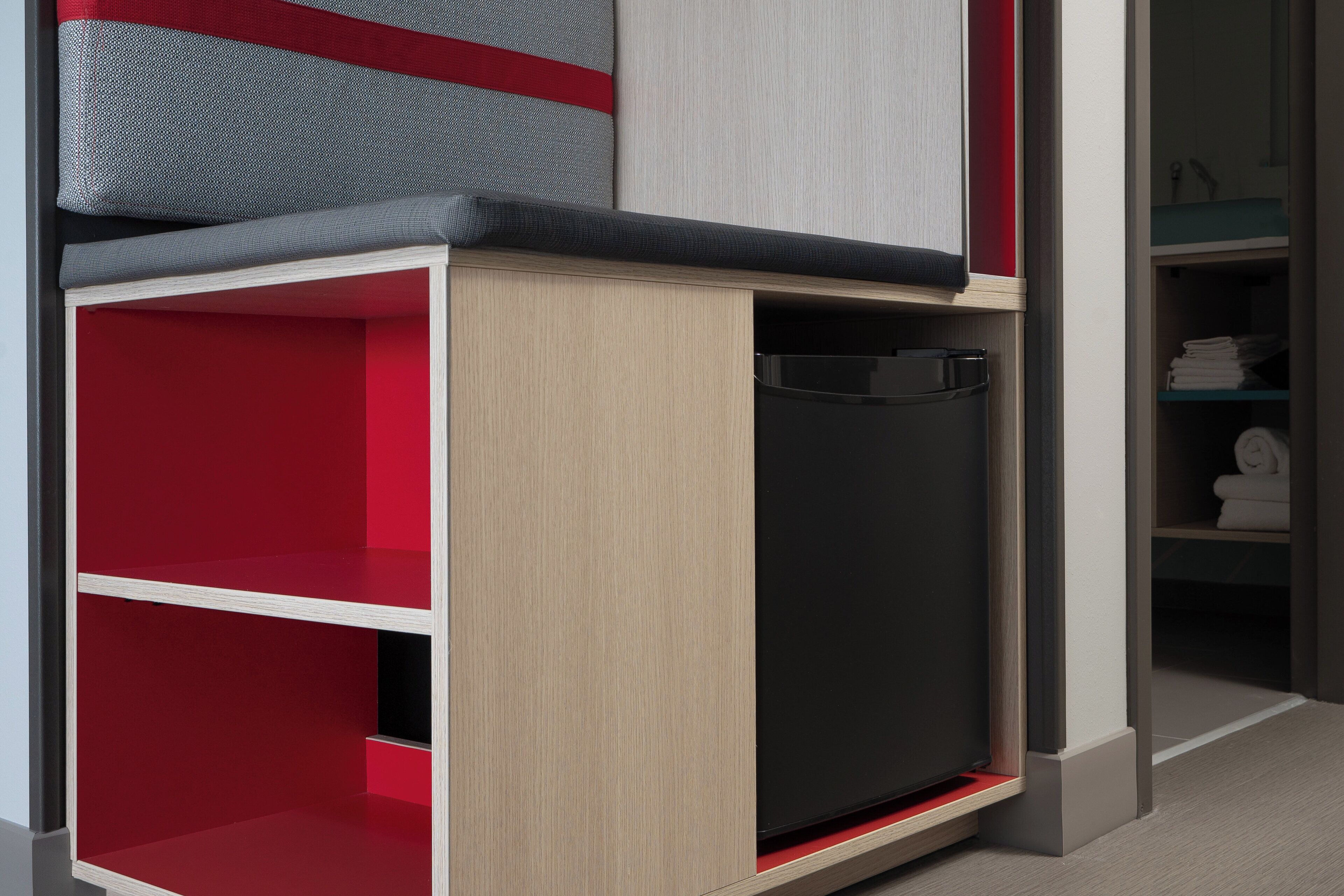 Une chambre moderne dotée d’un placard intégré, d’un appareil électroménager noir et d’une étagère rouge.