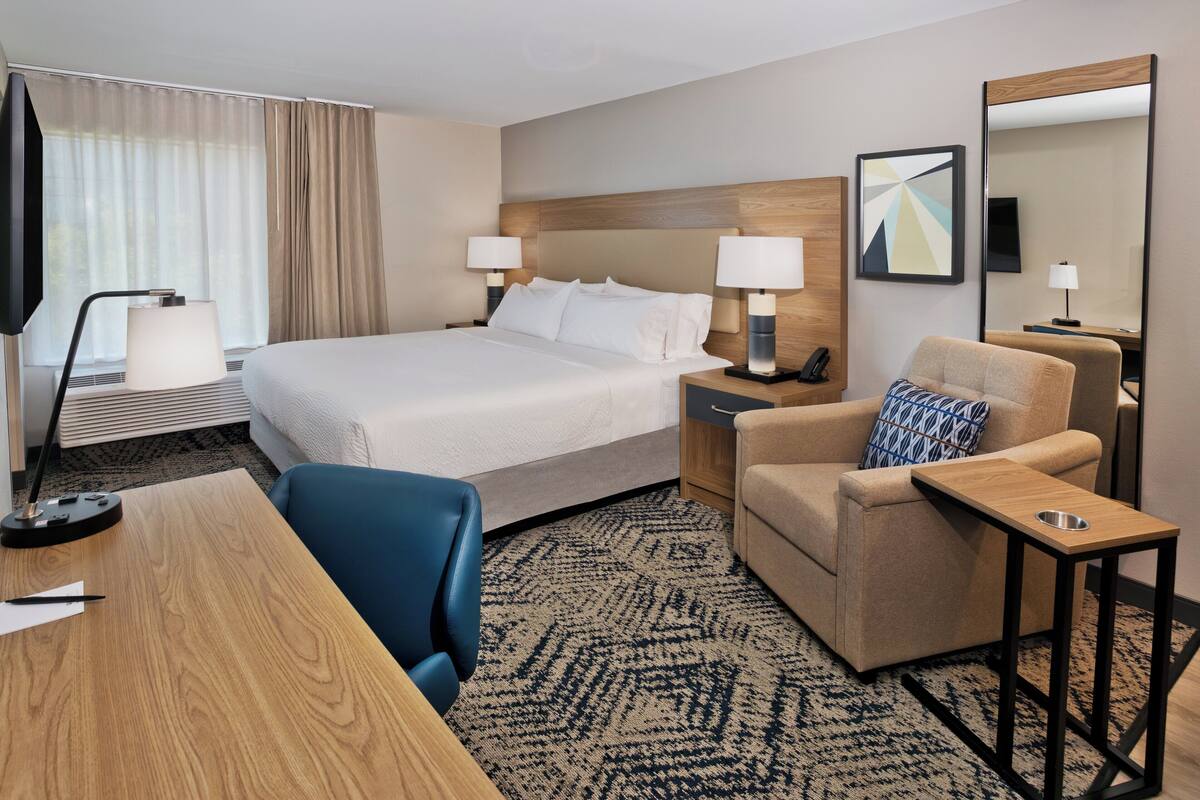 A hotel room with a large bed, two bedside tables with lamps, a desk with a chair, a sofa, and a small side table.