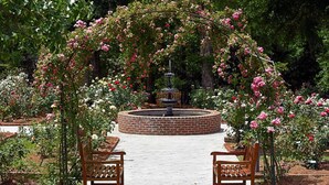 Ein Garten mit einem Ziegelbrunnen, Bänken und einem mit Blumen bewachsenen Pergola.