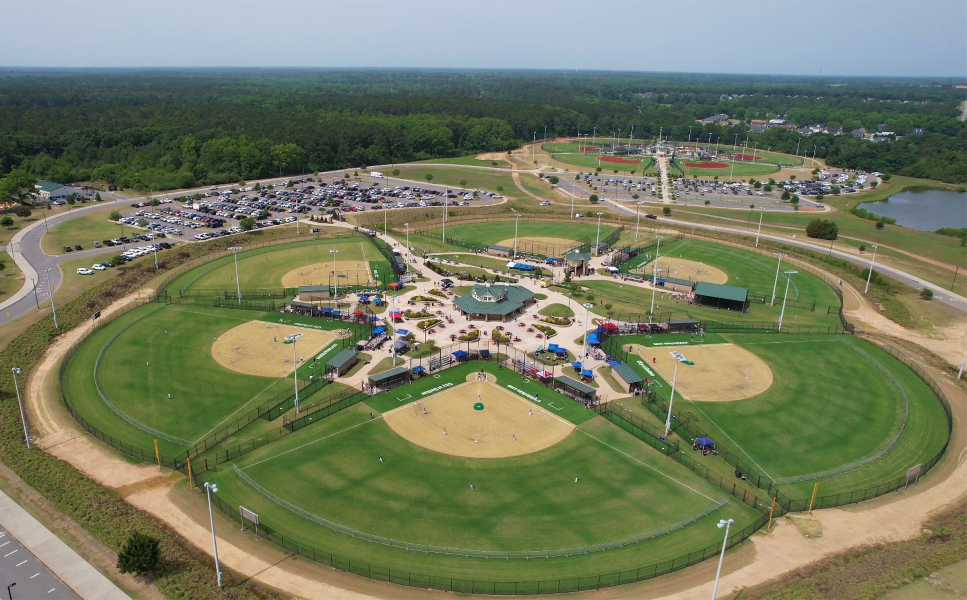 Vue aérienne d’un complexe sportif comprenant plusieurs terrains de baseball, des aires de stationnement et des espaces verts environnants.