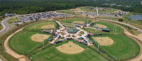Vue aérienne d’un complexe sportif comprenant plusieurs terrains de baseball, des aires de stationnement et des espaces verts environnants.
