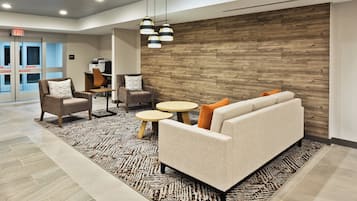Un lobby moderno con un sofá, sillas y una mesa de centro. Se observa una pared de madera y una alfombra estampada.