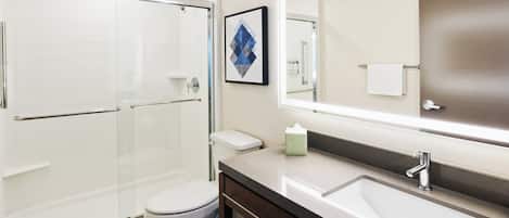 Un baño moderno con cabina de ducha de vidrio, inodoro blanco, un espejo grande y mueble de tocador doble.