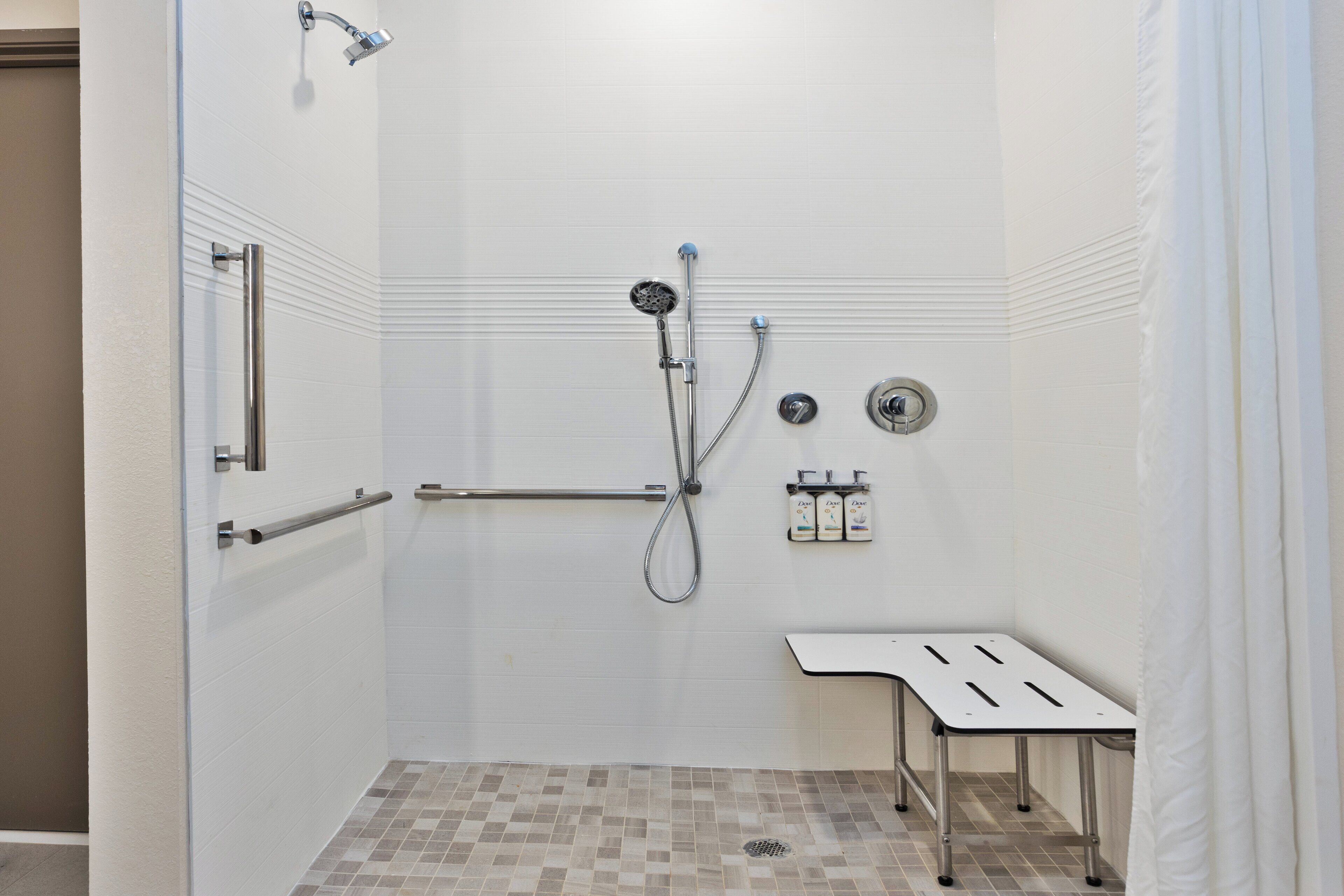 A shower with a handheld showerhead, a handheld shower nozzle, and a wall-mounted faucet. There is a bench and a towel rack.
