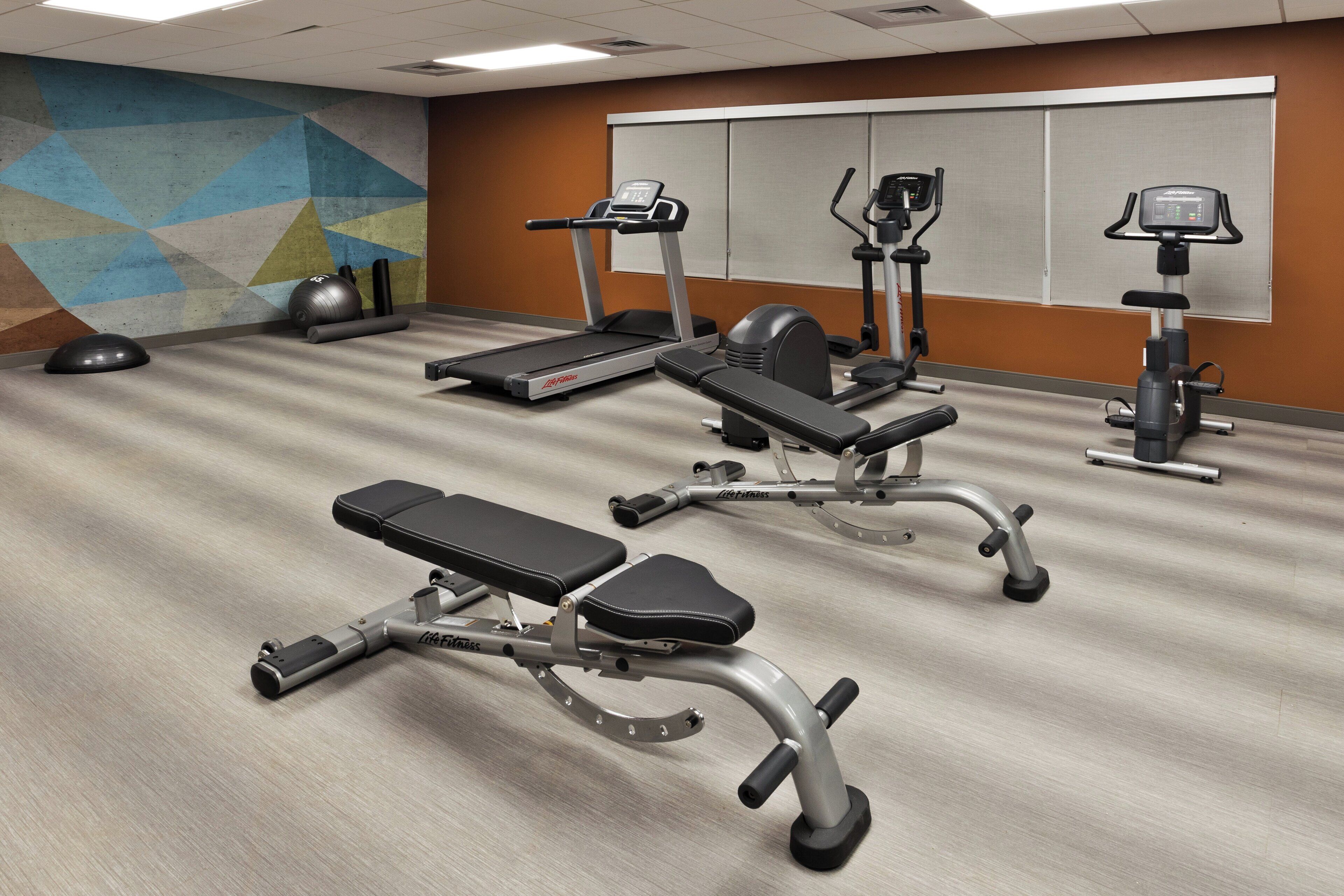 Ein Fitnessstudio mit Laufbändern, Crosstrainern und Gewichtsbänken.