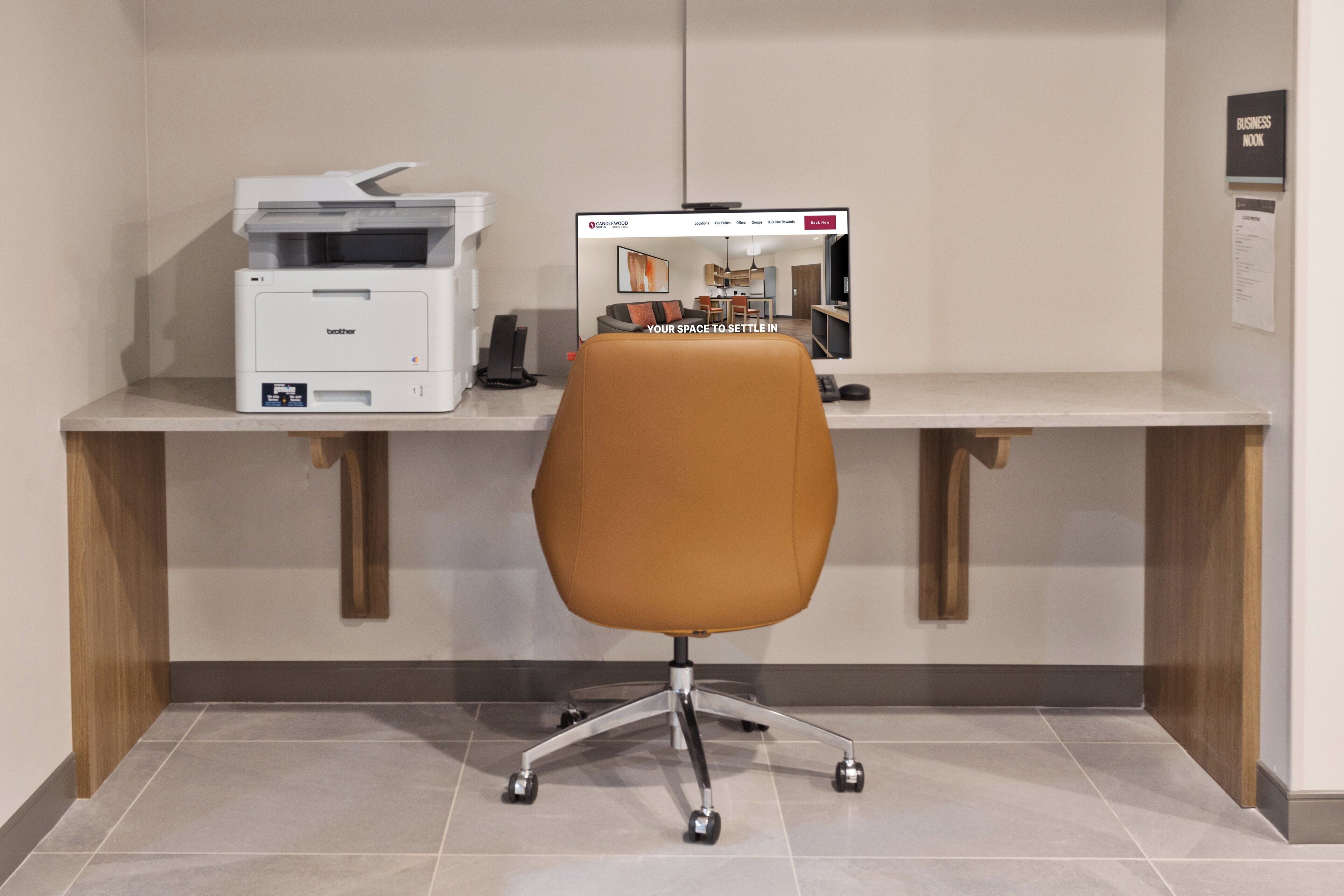 Um espaço de escritório moderno com uma mesa, uma impressora e um monitor de computador exibindo um site imobiliário.
