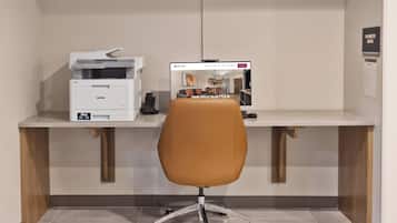 Um espaço de escritório moderno com uma mesa, uma impressora e um monitor de computador exibindo um site imobiliário.