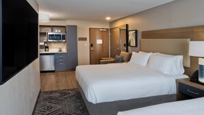 Ein Hotelzimmer mit einem großen Bett, einem Nachttisch, einem Schreibtisch, einer Mikrowelle, einer Kaffeemaschine und einer kleinen Sitzecke.