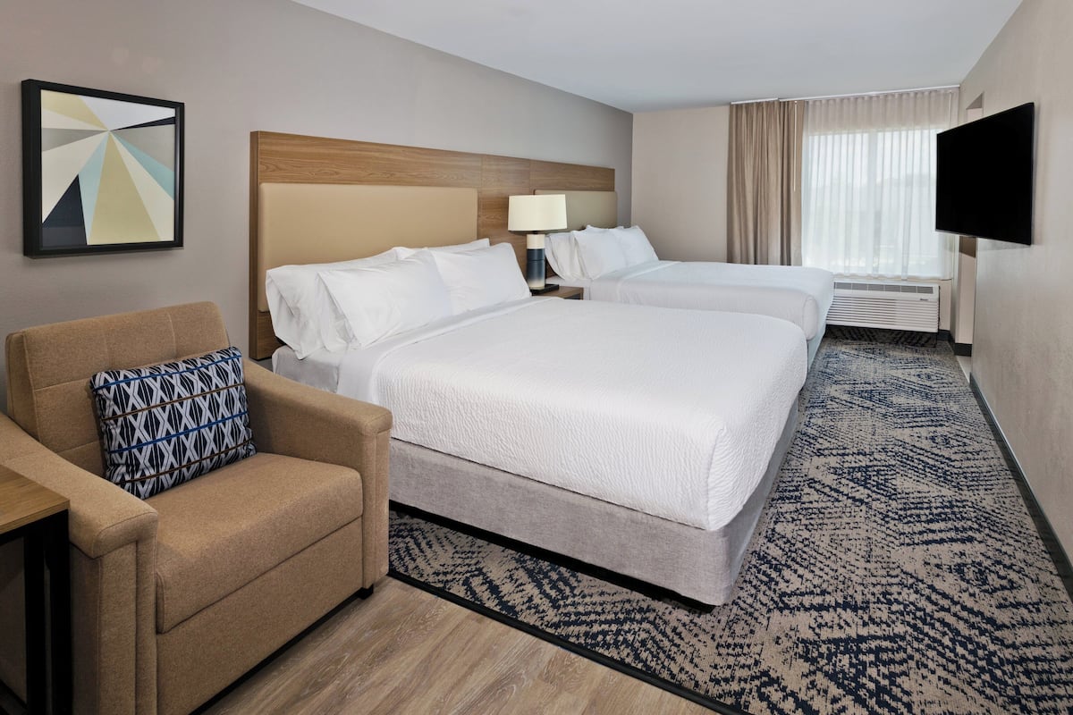 A hotel room with two beds, a sofa, a TV, and a large window with curtains.