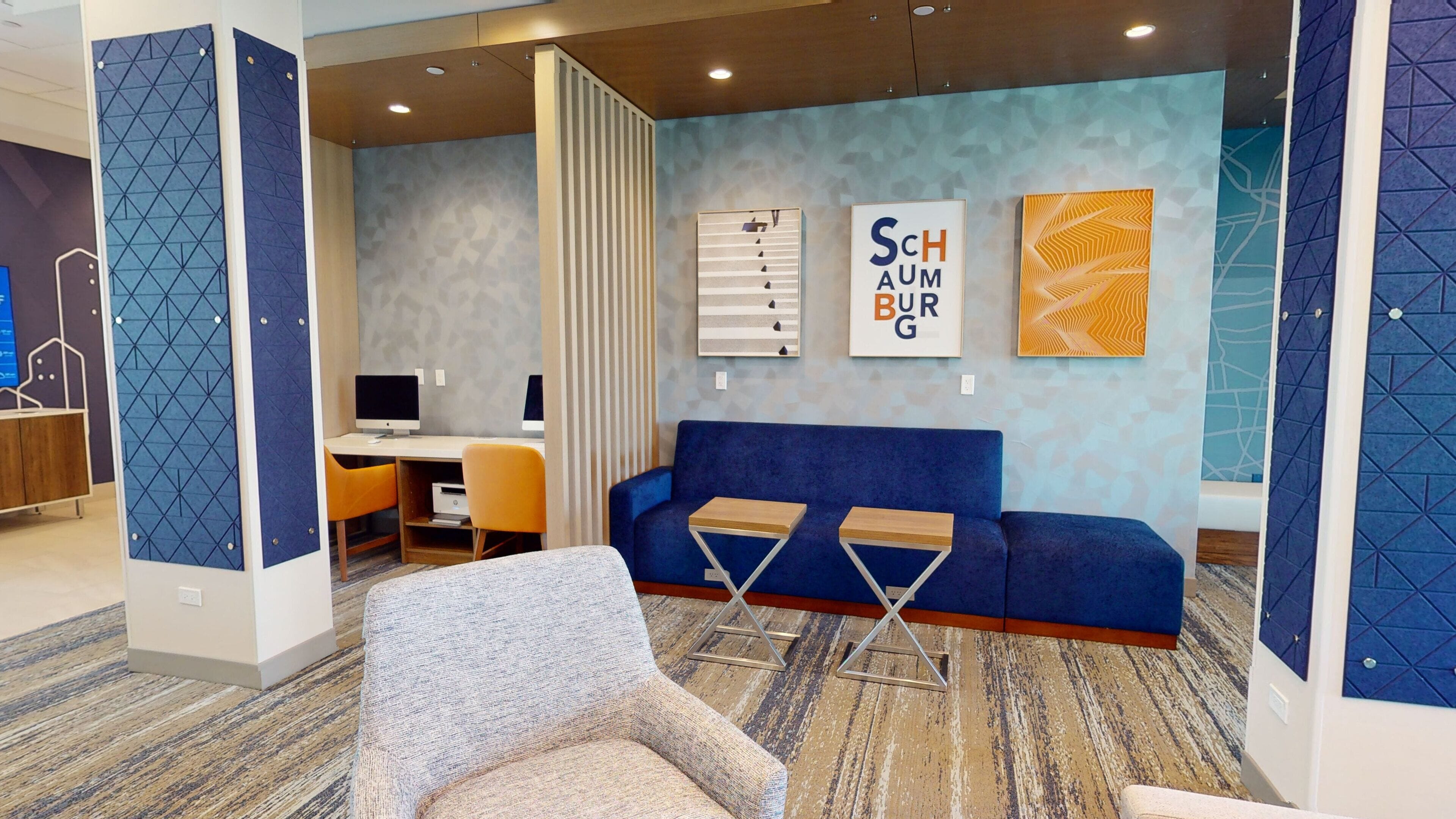 Ein moderner Büroraum mit einem blauen Sofa, zwei Schreibtischen mit Computern und einem gemusterten Teppich.