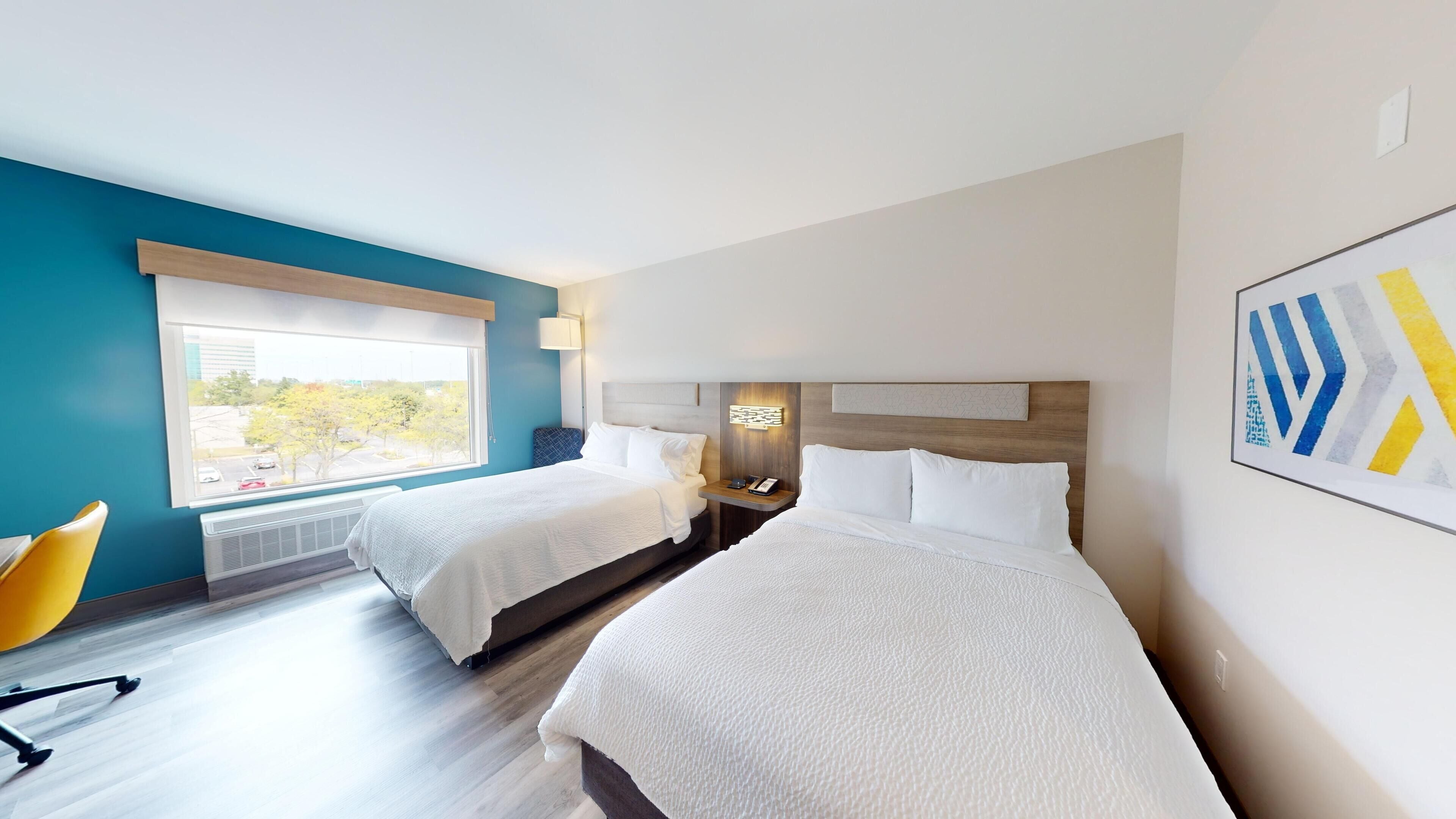 Une chambre d’hôtel avec deux lits, une fenêtre donnant sur un paysage agréable, une chaise et une œuvre d’art accrochée au mur.