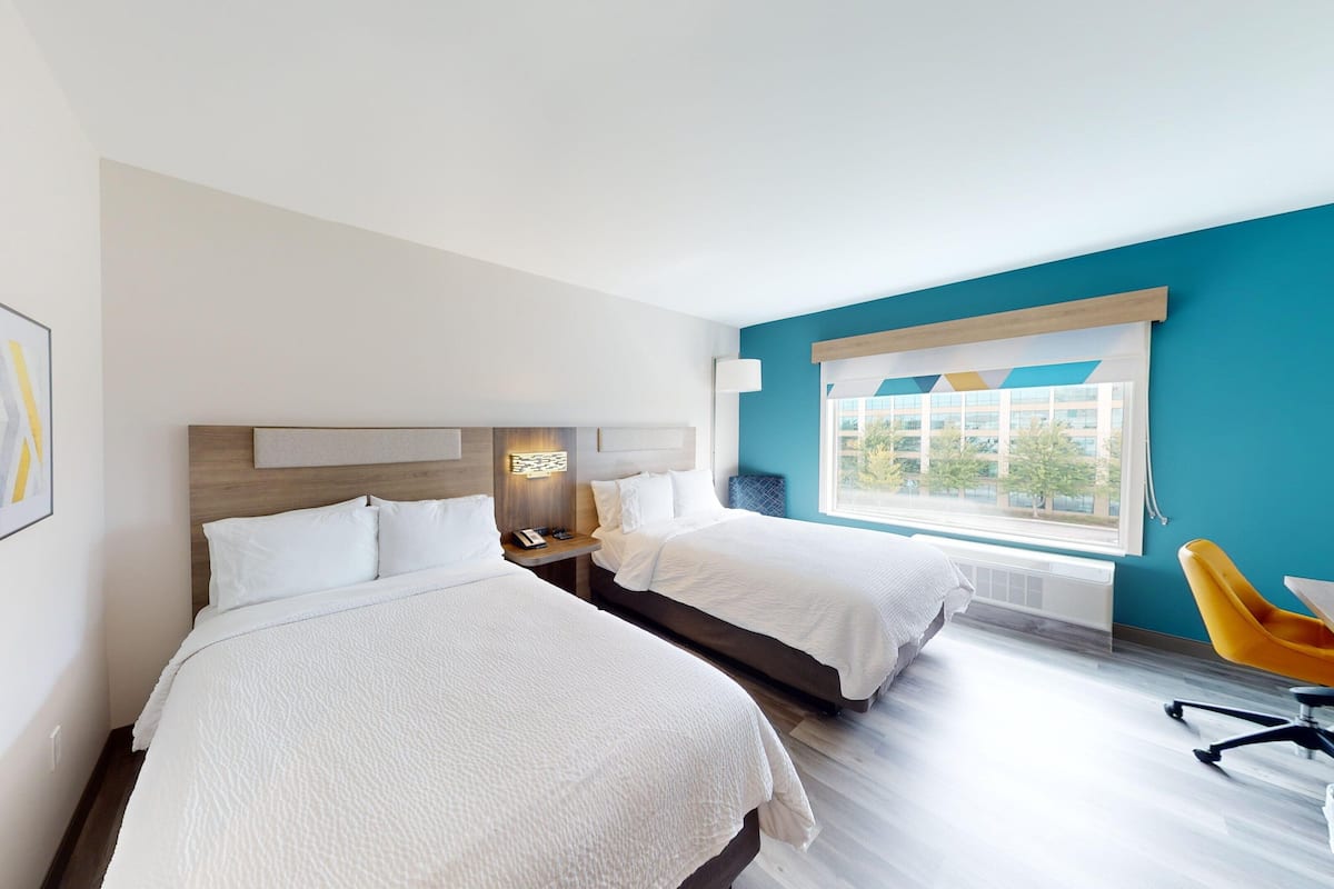 A hotel room with two beds, a large window with a view, and a yellow chair.