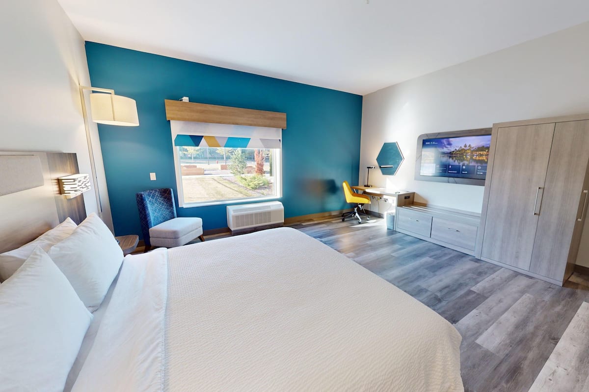 A modern hotel room with a large bed, a desk, a chair, and a wardrobe.