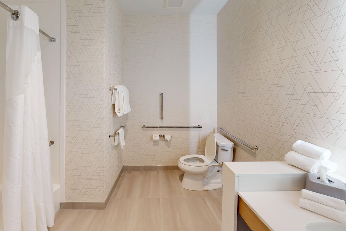 Features a shower, toilet with grab bar, and sink area with towel dispenser.