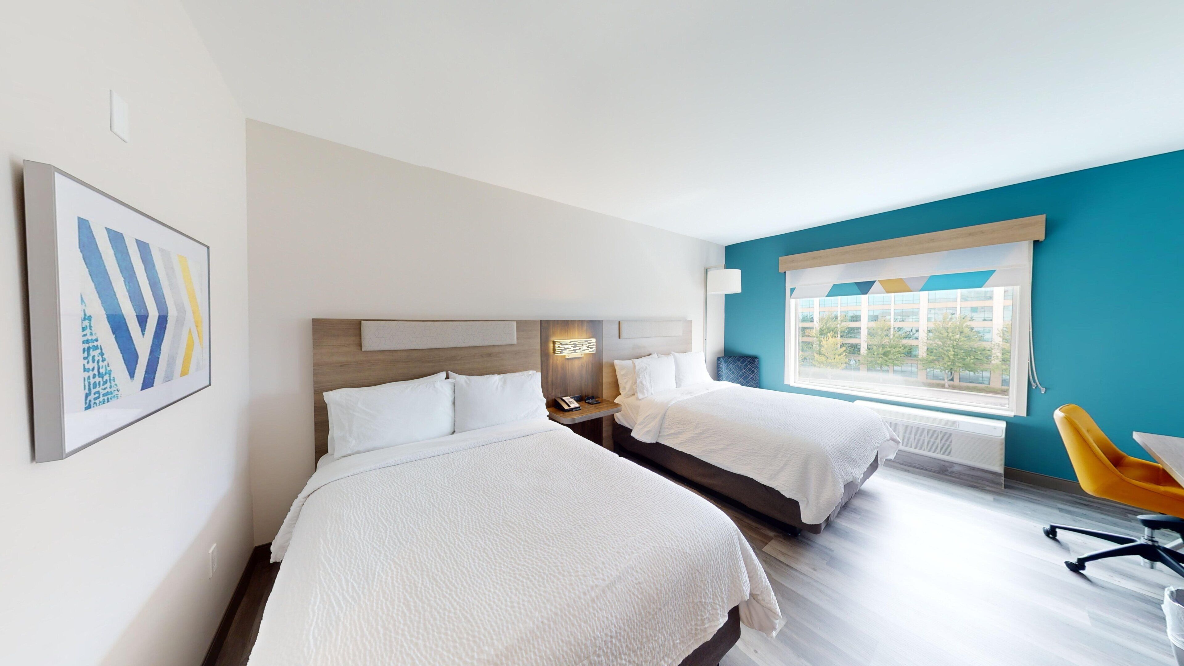 A hotel room with two beds, a large window with a view, and a yellow chair.