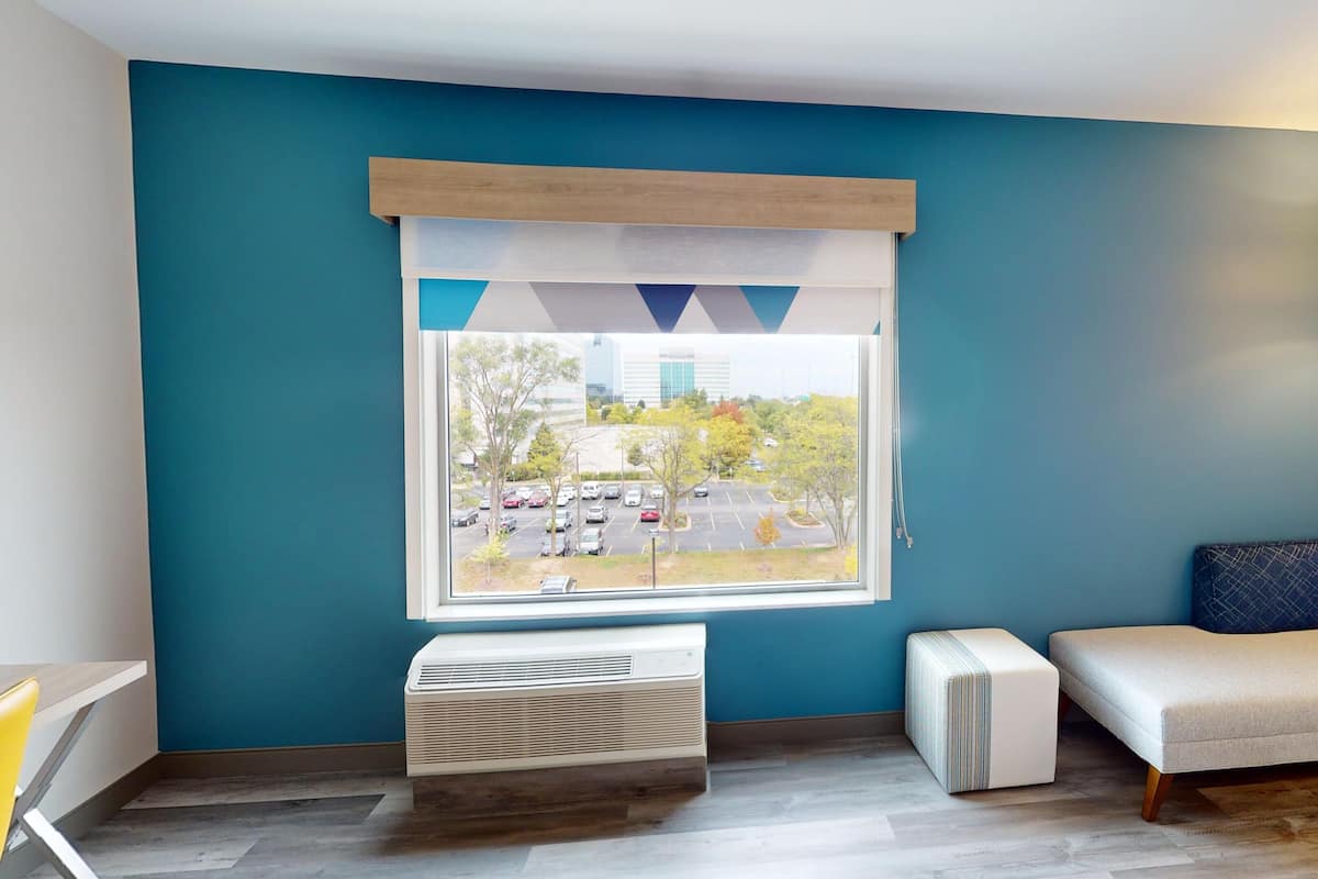 Enjoy a comfortable stay with a large window offering a view of the surrounding area, a bed, and a bedside table with a lamp.