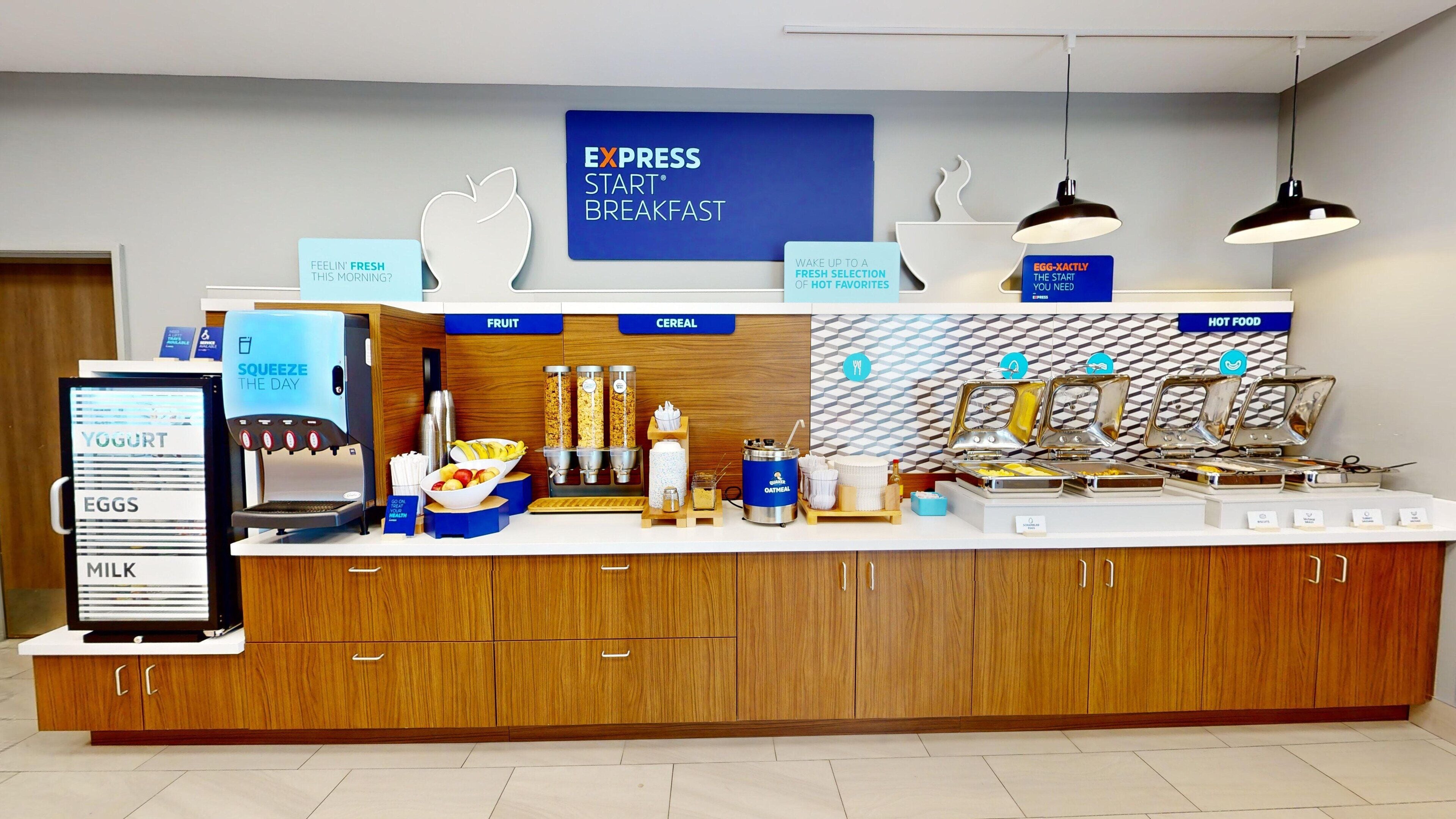 A breakfast station with a digital menu board, yogurt, eggs, milk, a coffee machine, fruit, cereal, and hot food options.
