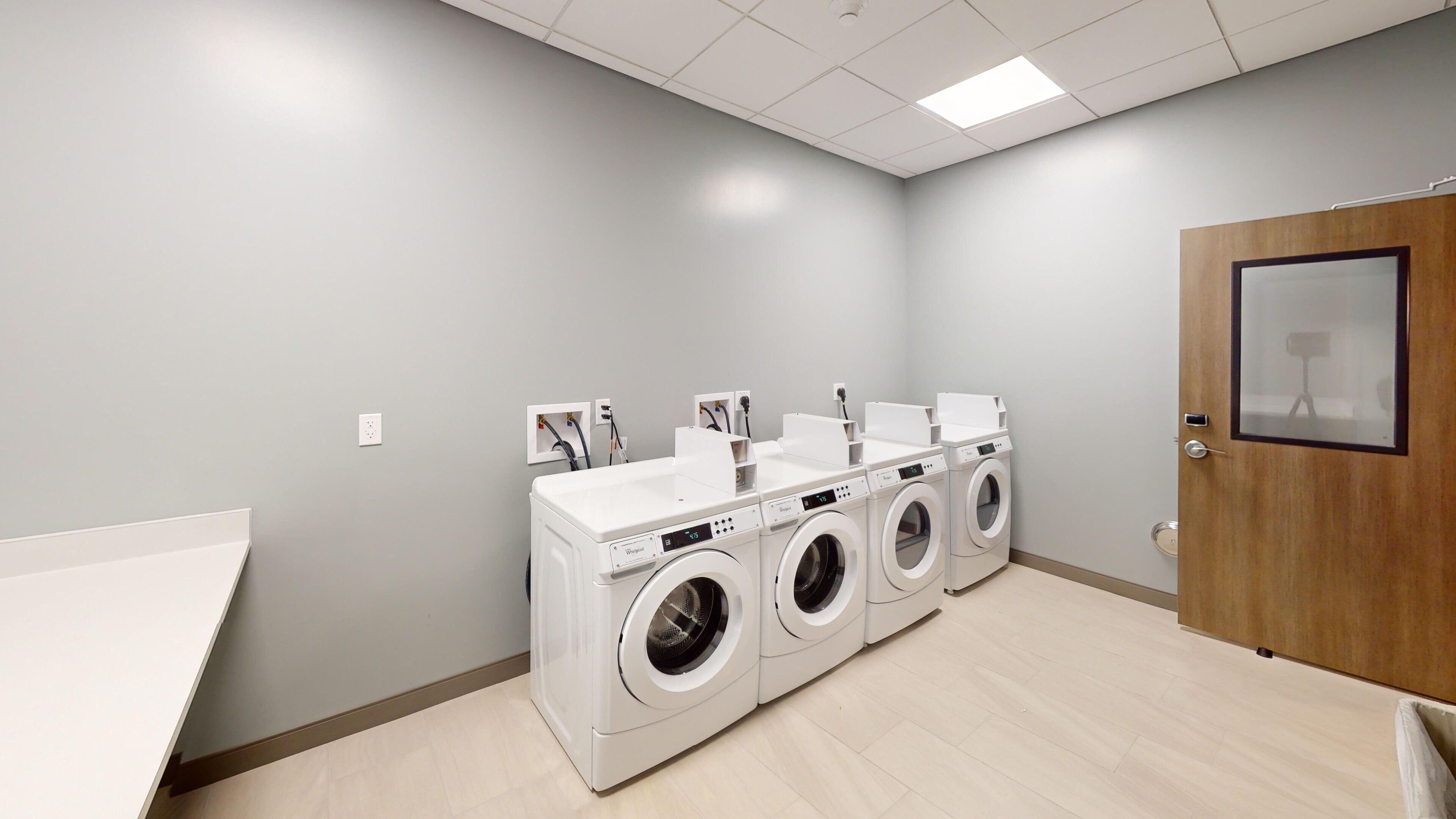 A laundry facility with three front-loading washing machines and two sinks.