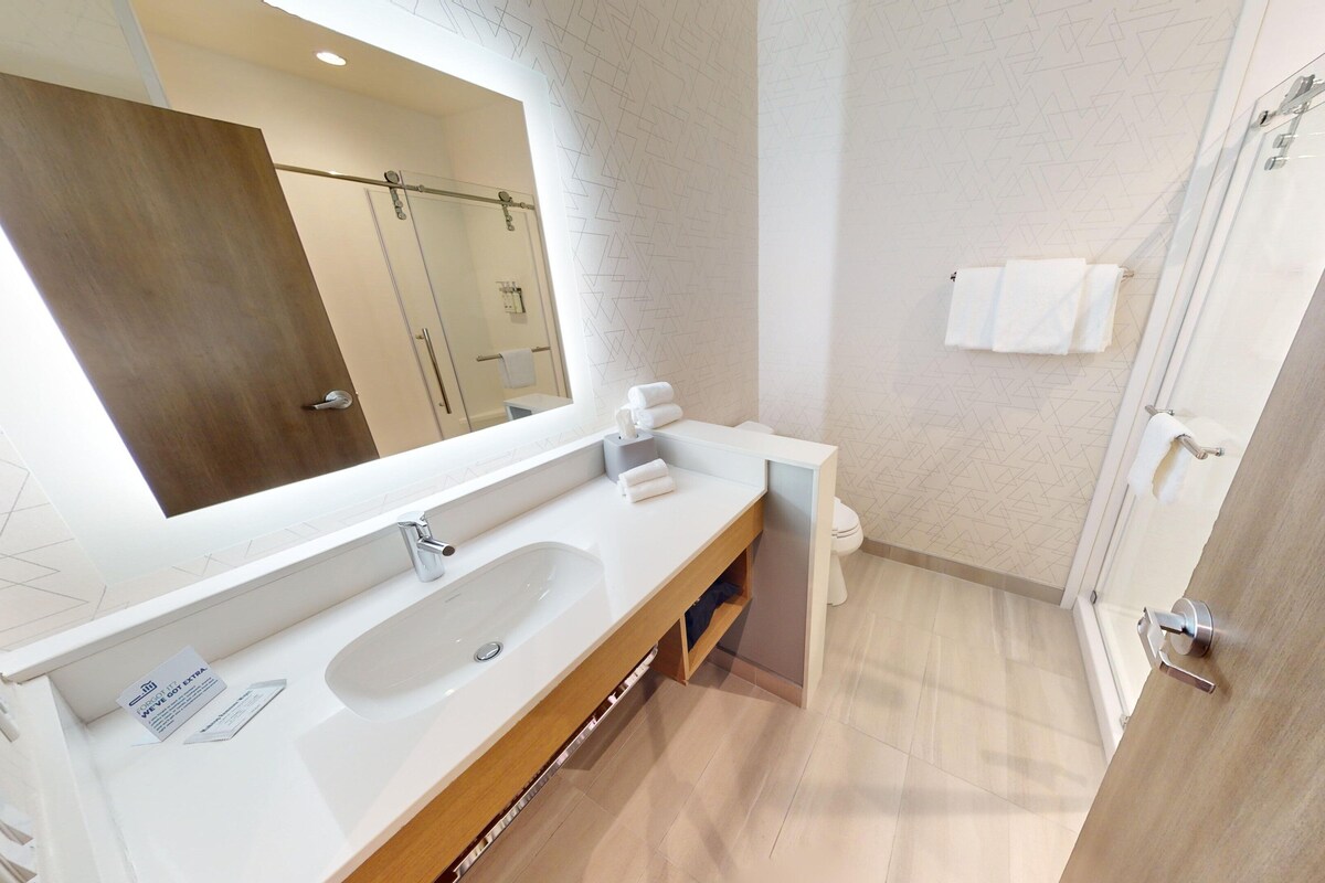 A modern bathroom with a large mirror, a double sink, and a shower area.