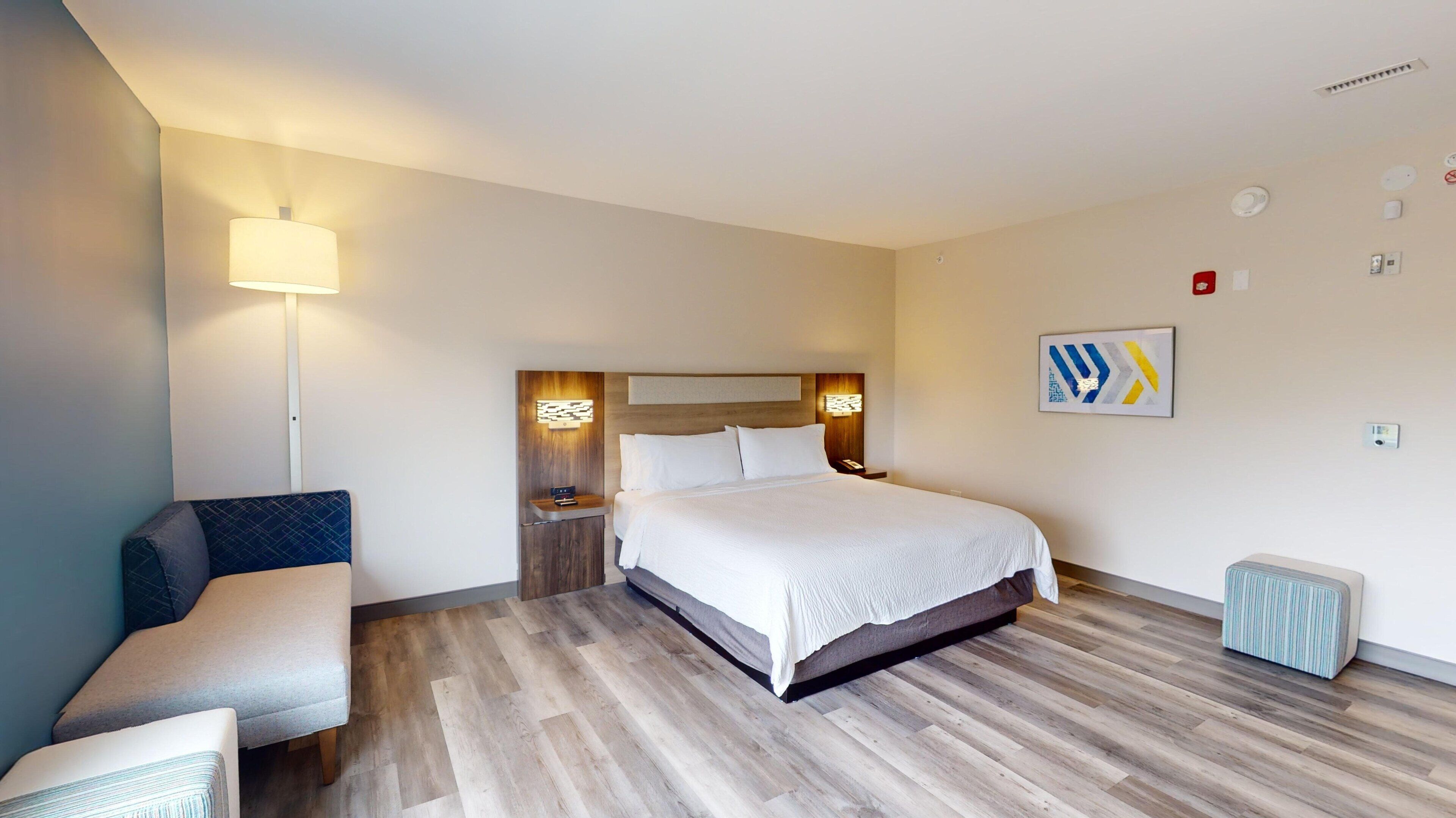 A hotel room with a bed, bedside tables, a lamp, a chair, and a small stool.