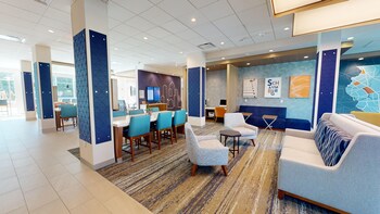 A hotel lobby with a reception desk, seating area, and a television screen. at Holiday Inn Express & Suites Chicago Schaumburg by IHG