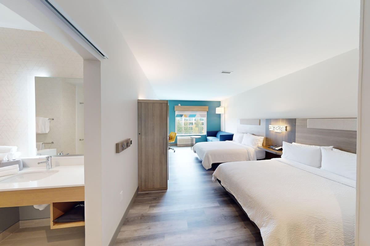 A hotel room with a bathroom, a bed, a desk, and a window.
