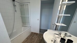 Une salle de bain moderne avec un plancher en bois, une baignoire blanche, un lavabo avec un miroir et une pomme de douche.