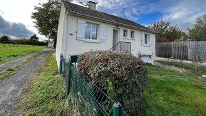 Une maison de plain-pied avec un toit en tuiles, un petit porche et une clôture verte.