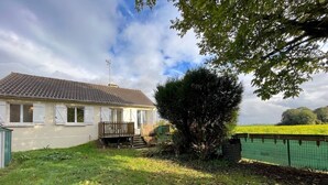 Une maison avec un toit en tuiles, une terrasse en bois et un jardin clos.
